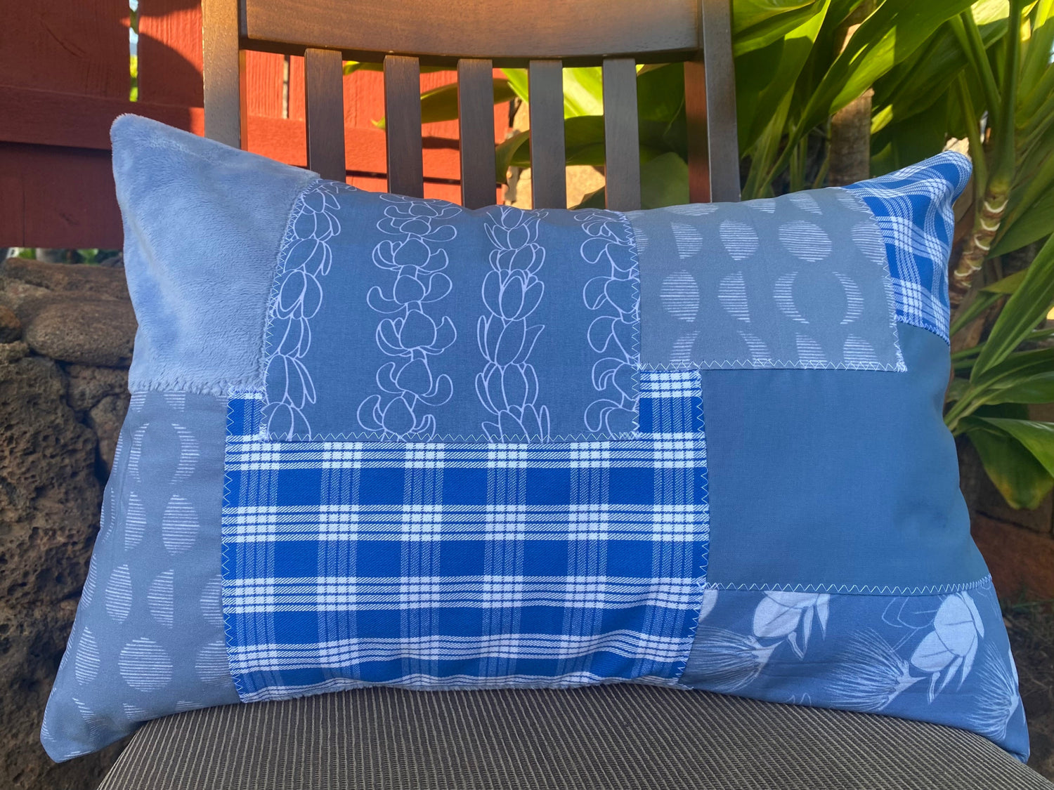 Blue local hawaiian handmade patchwork pillow on a chair with a blurred outdoor background