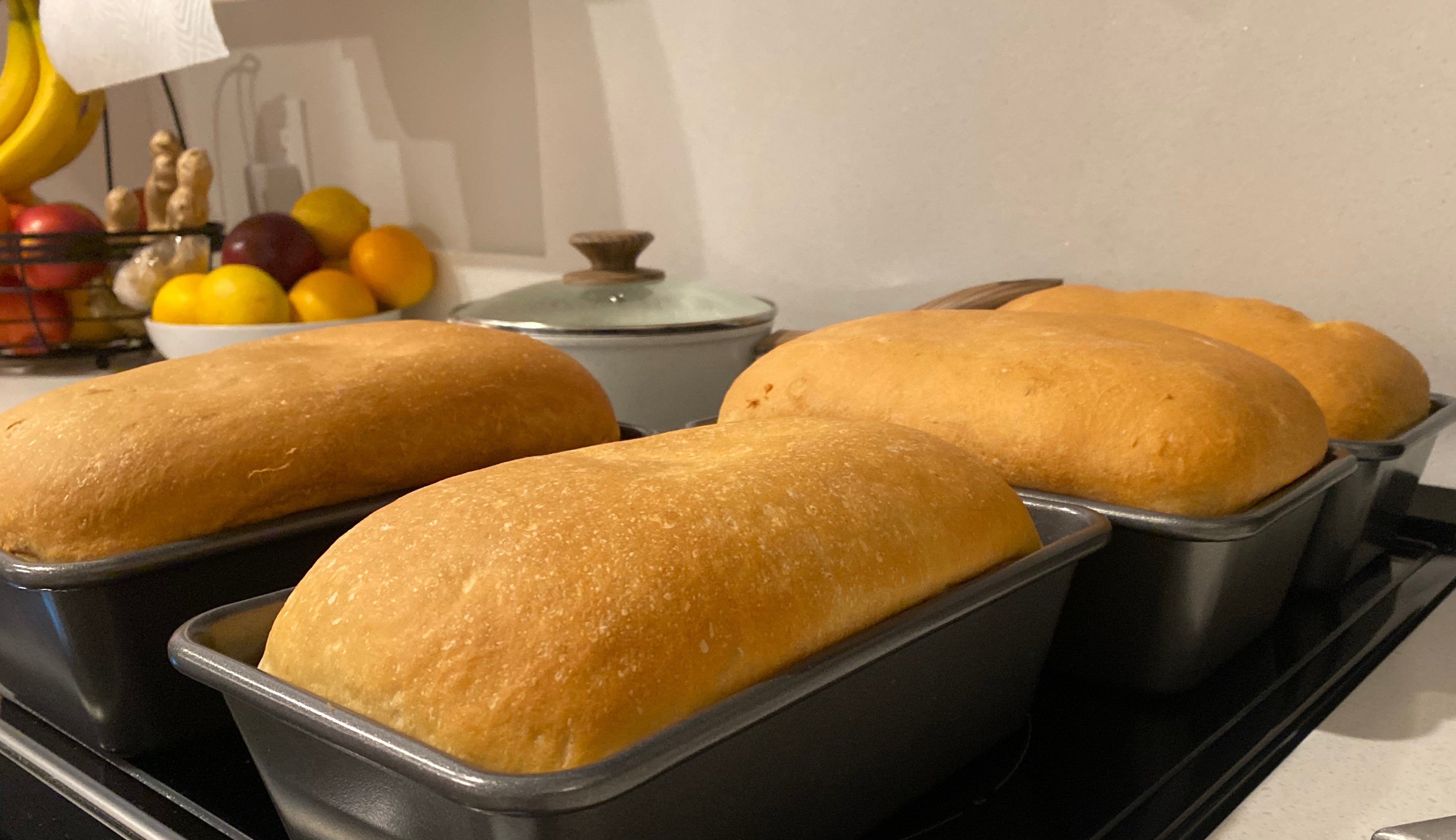 Loaves of bread in loaf pans on a kitchen counter with fruits in the background